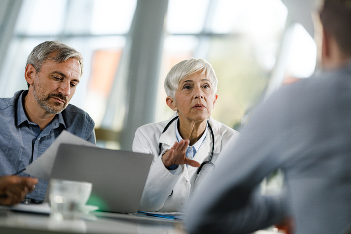 Female medical expert communicating with businessmen while having a meeting at doctor's office in the hospital.